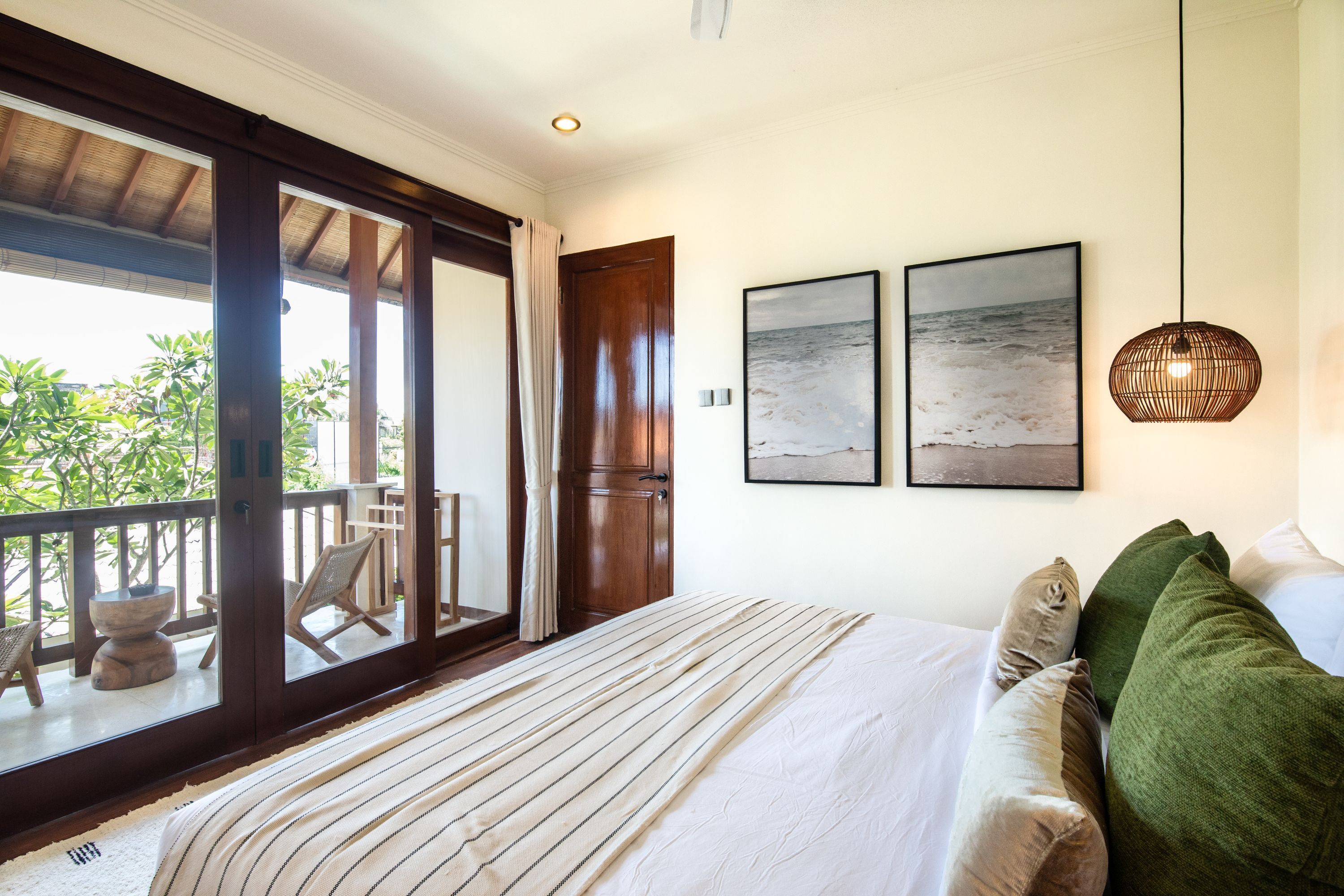 A bedroom with a large bed, a view of the outdoors, and two framed pictures on the wall.