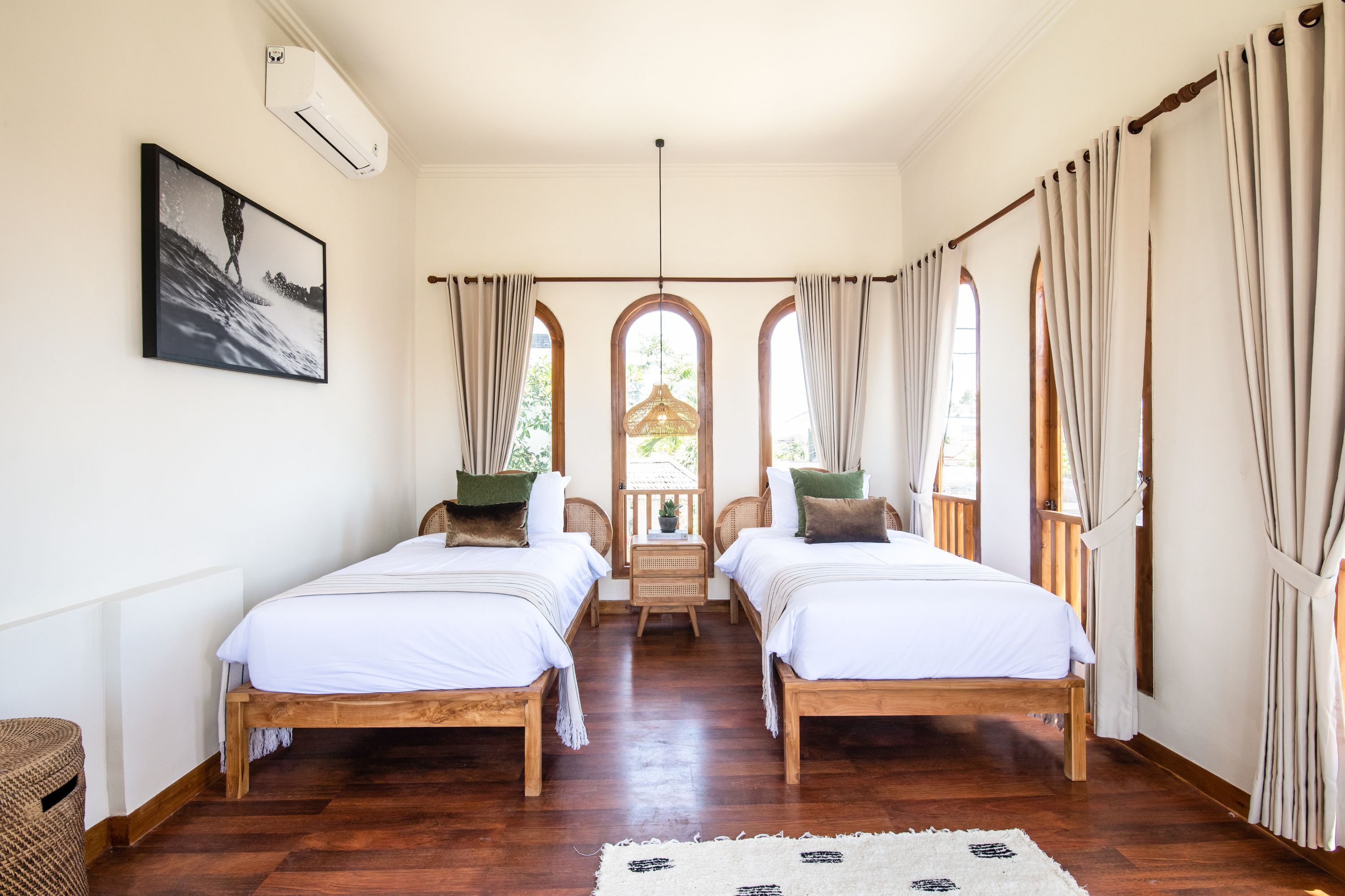 A room with two wooden beds, a rattan chair, a small table with a plant, and a framed picture on the wall.
