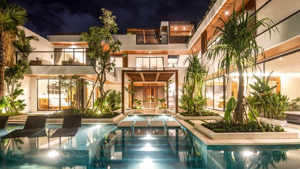 A modern outdoor pool area with lounge chairs, surrounded by tropical plants and a multi-level building with large windows. - Swastamita in Dalung (Canggu)