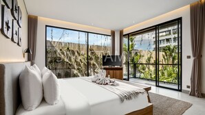 A modern bedroom with a large bed, a wooden headboard, and a view of a wooden fence and greenery outside. - Swastamita in Dalung (Canggu)