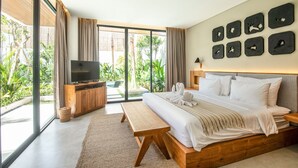 A modern bedroom with a large bed, a TV, and a view of greenery through large windows. - Swastamita in Dalung (Canggu)