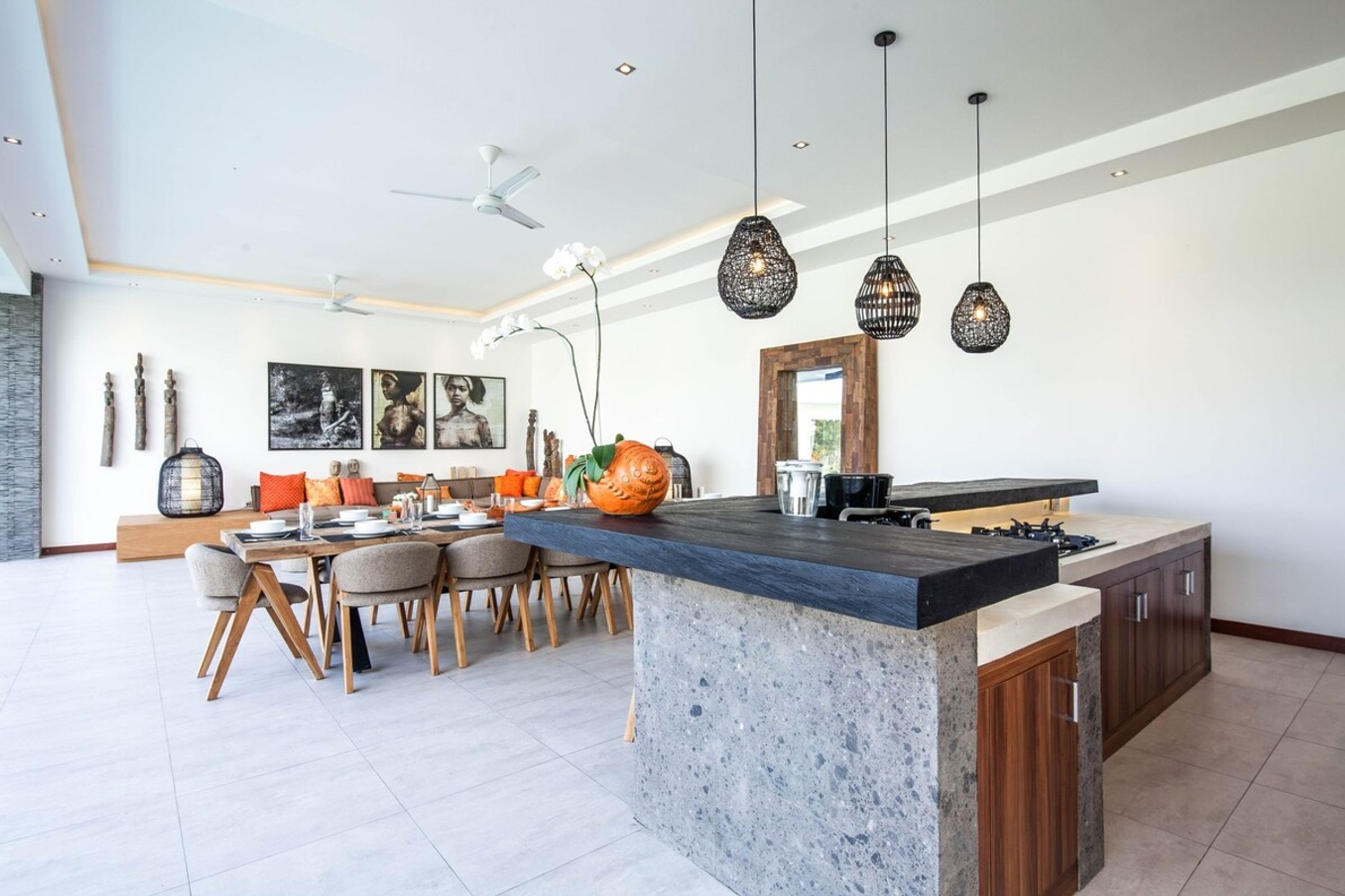 A modern kitchen with a central island, pendant lighting, and a dining area with a sofa and chairs.