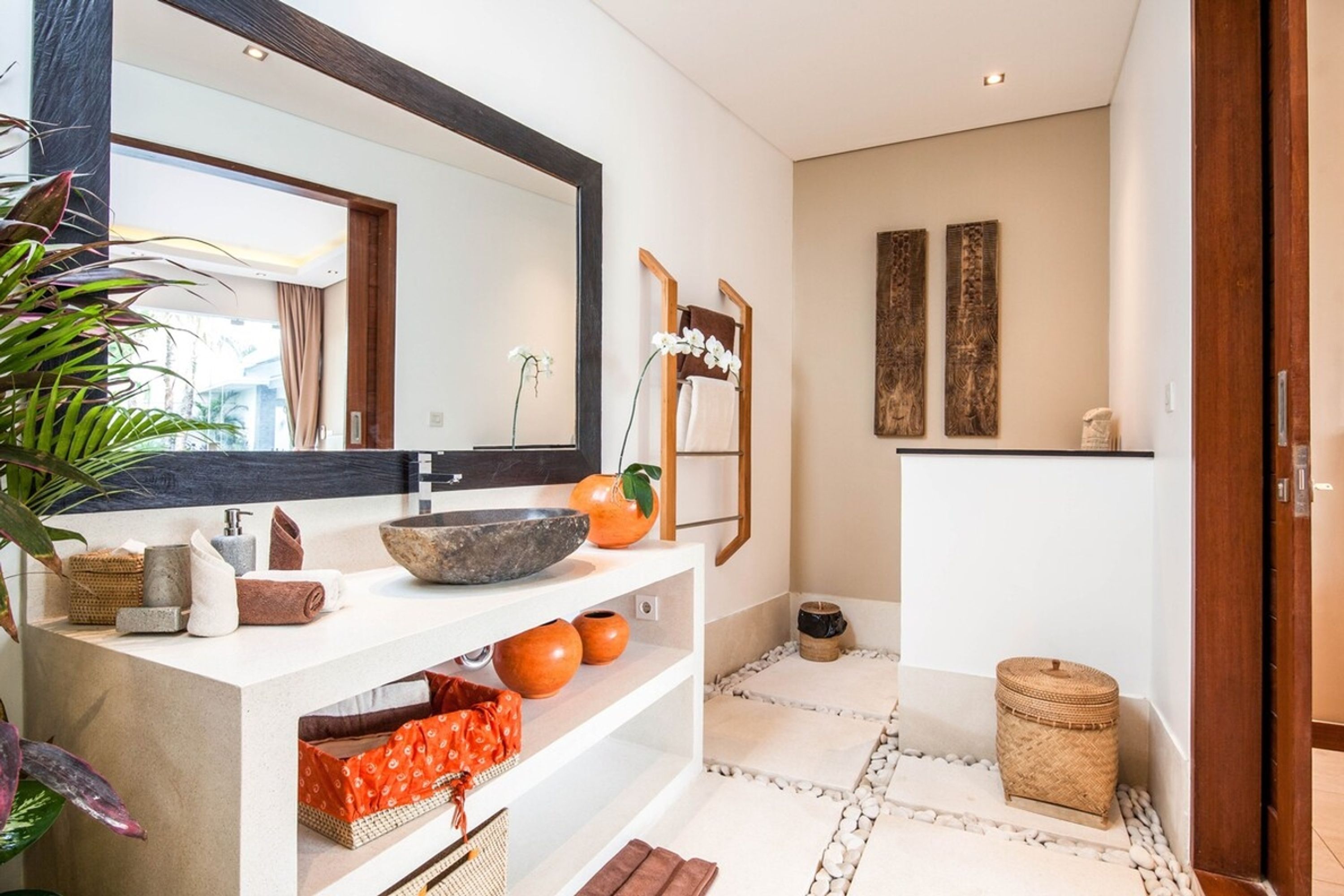 A modern bathroom with a large mirror, a stone basin, and various toiletries on shelves.