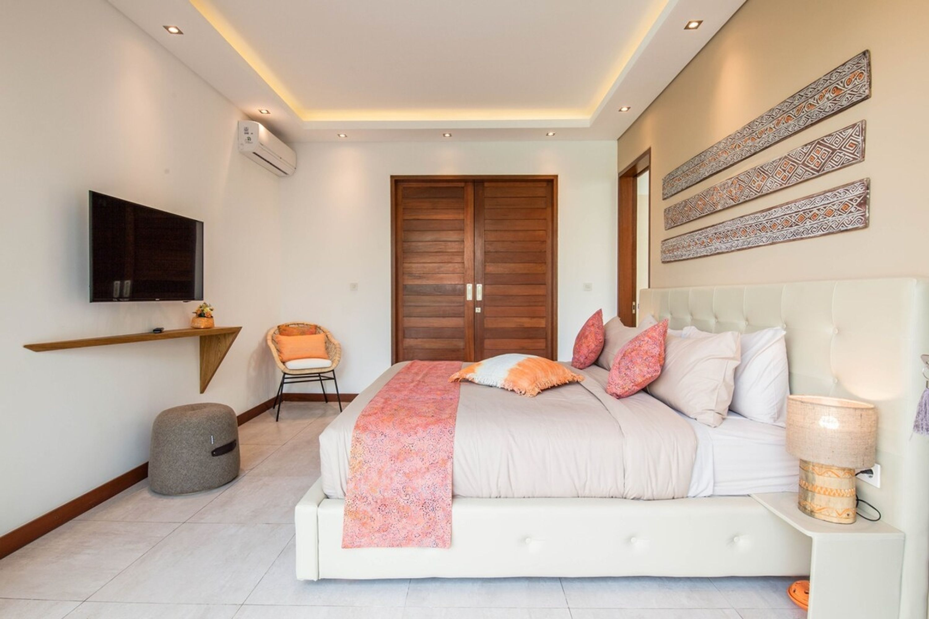 A modern bedroom with a large bed, a television mounted on the wall, a wardrobe, and decorative wall art.