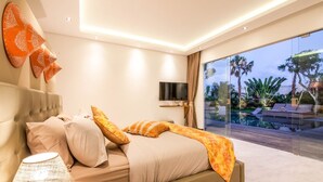 Ein modernes Schlafzimmer mit Bett, Fernseher und Blick auf Pool und Außenbereich.