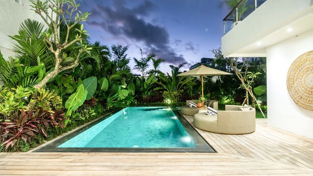 A modern outdoor pool area with a wooden deck, surrounded by lush tropical plants and a large umbrella. - Sol N3 S in Dalung (Tibubeneng)