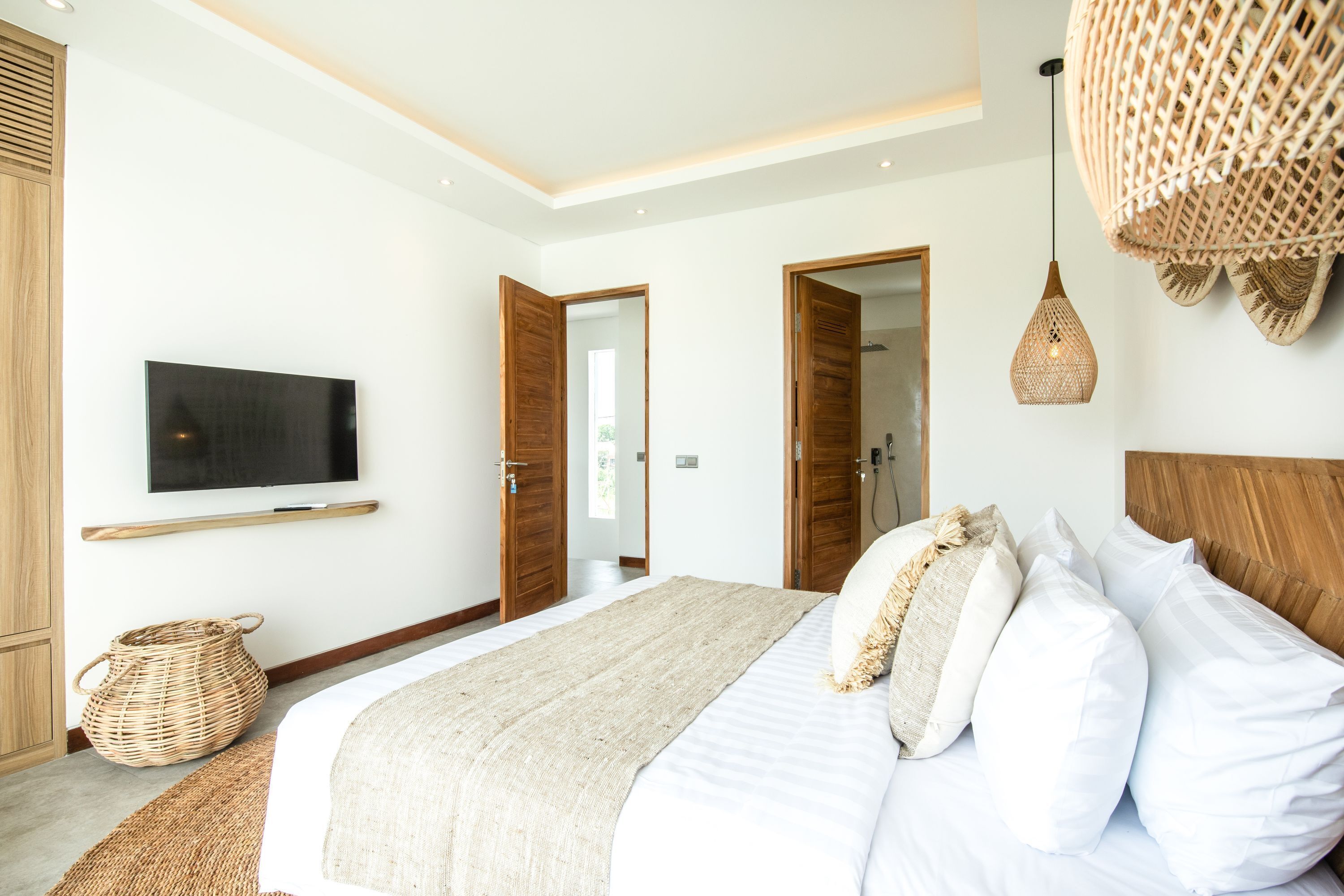 Une chambre moderne avec un grand lit, des portes en bois, un téléviseur à écran plat et un panier en osier.