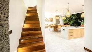A modern kitchen with a wooden staircase, a dining area, and a living space with a large plant and pendant lights. - Sol N3 S in Dalung (Tibubeneng)