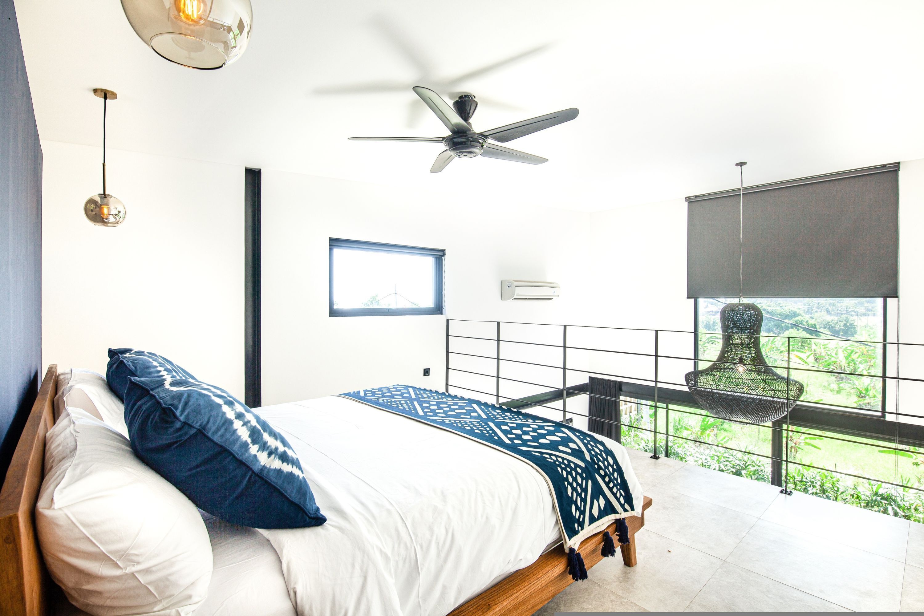 Une chambre avec un lit, un ventilateur de plafond, une fenêtre donnant sur un beau paysage et un fauteuil suspendu.