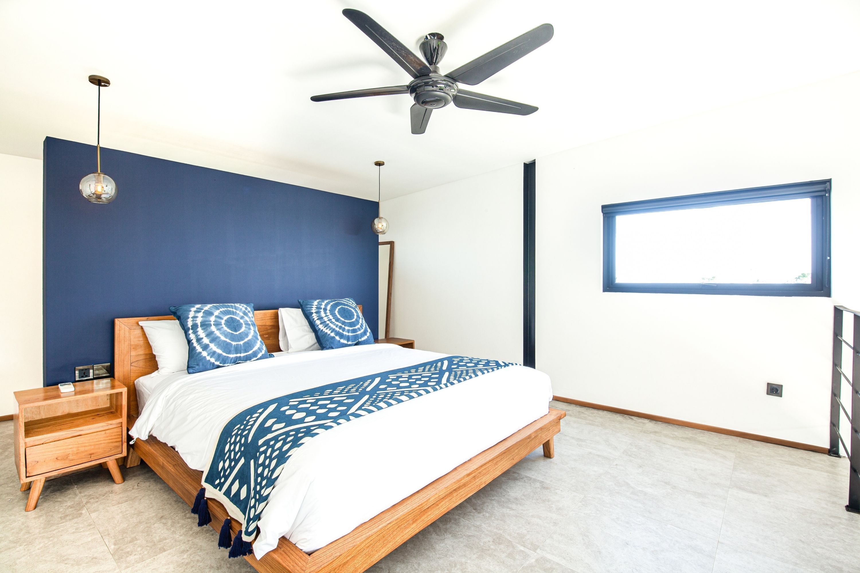 A bedroom with a bed, nightstands, a ceiling fan, a window, and a view of the outdoors.