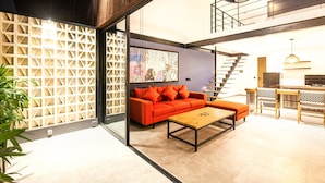 A modern living room with a sofa, coffee table, and chairs, a staircase leading to an upper level, and a kitchen area. - Loft 1 App in Pererenan (Munggu)