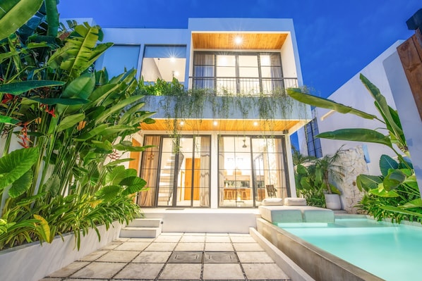 Una casa moderna con piscina, ventanas amplias y abundante vegetación.