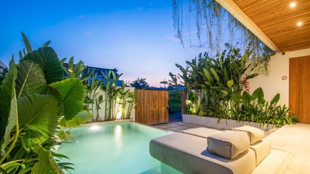 Ein Poolbereich im modernen Stil mit Holzboden, umgeben von üppigen tropischen Pflanzen und einem beigen Sofa.