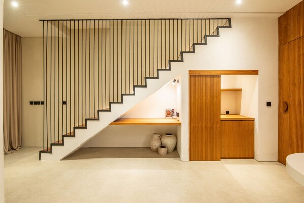 Un interior moderno con una escalera que lleva a una puerta de madera, un pequeño estante con adornos y un piso de baldosas.