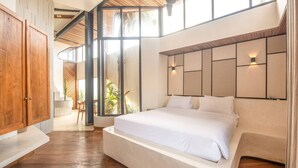 Un dormitorio moderno con una cama grande, suelo de madera y vistas a la vegetación a través de amplias ventanas.