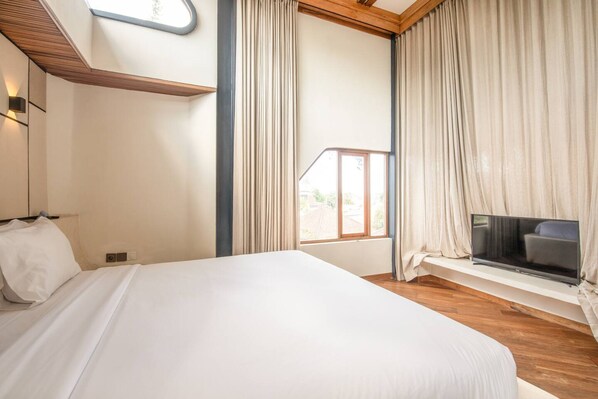 A bedroom with a large bed, a TV on a built-in shelf, and a window with curtains.