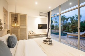 A bedroom with a large bed, a TV, a window with a view of a swimming pool and greenery, and a wooden ceiling. - Canggu KOI 5 Villa in Canggu (Canggu)