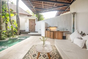 Un espacio exterior moderno con piscina, sofá, una mesita y una zona de cocina.