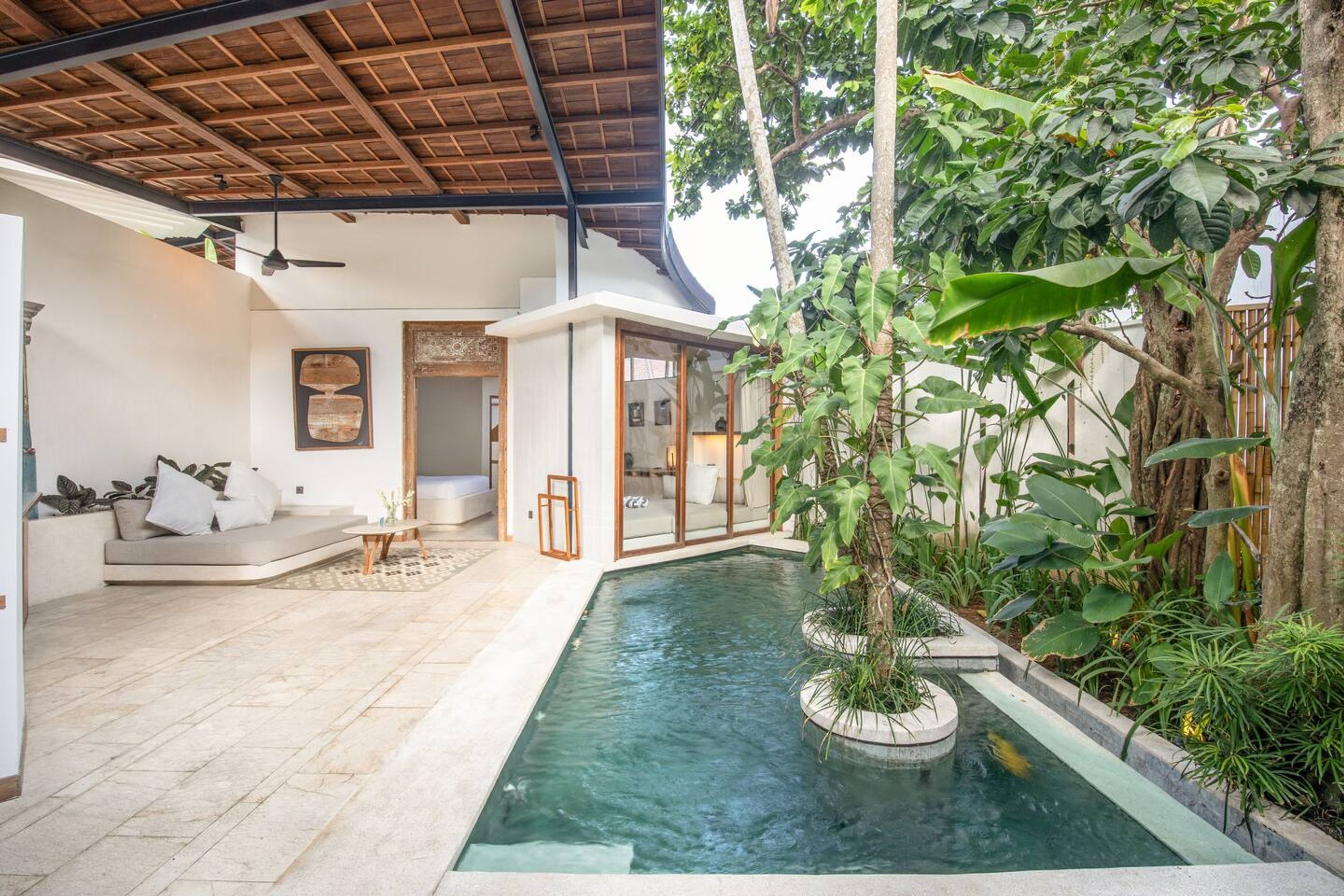 A modern indoor pool area with a glass enclosure, surrounded by lush greenery and a wooden ceiling.