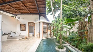 Un área de piscina interior moderna con cerramiento de vidrio, rodeada de exuberante follaje y techo de madera.