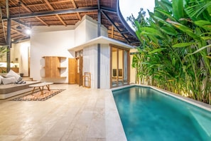 A modern indoor pool area with a clear view of the pool, a wooden deck, and a seating area with cushions. - BA Villa 4 1BR Lush 1-br Villa With Pool 4 Mins to Echo Beach (Canggu)