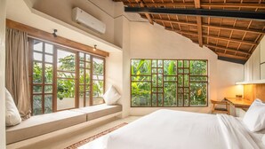 A bedroom with a large bed, a window with a view of greenery, a built-in bench, and a ceiling fan. - BA Villa 10 2 BR Stylish 2-br Villa With Pool 800m Canggu Beach (Pererenan)