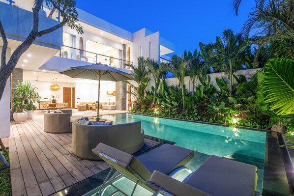 Un espace piscine extérieur moderne, doté de chaises longues et d’une terrasse en bois.
