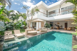 Une maison moderne dotée d’une grande piscine, d’un espace salon extérieur et d’une végétation luxuriante.