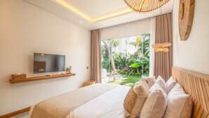 A bedroom with a large bed, a television on a shelf, and a view of greenery outside. - SOL n2 Villa in Dalung (Tibubeneng)