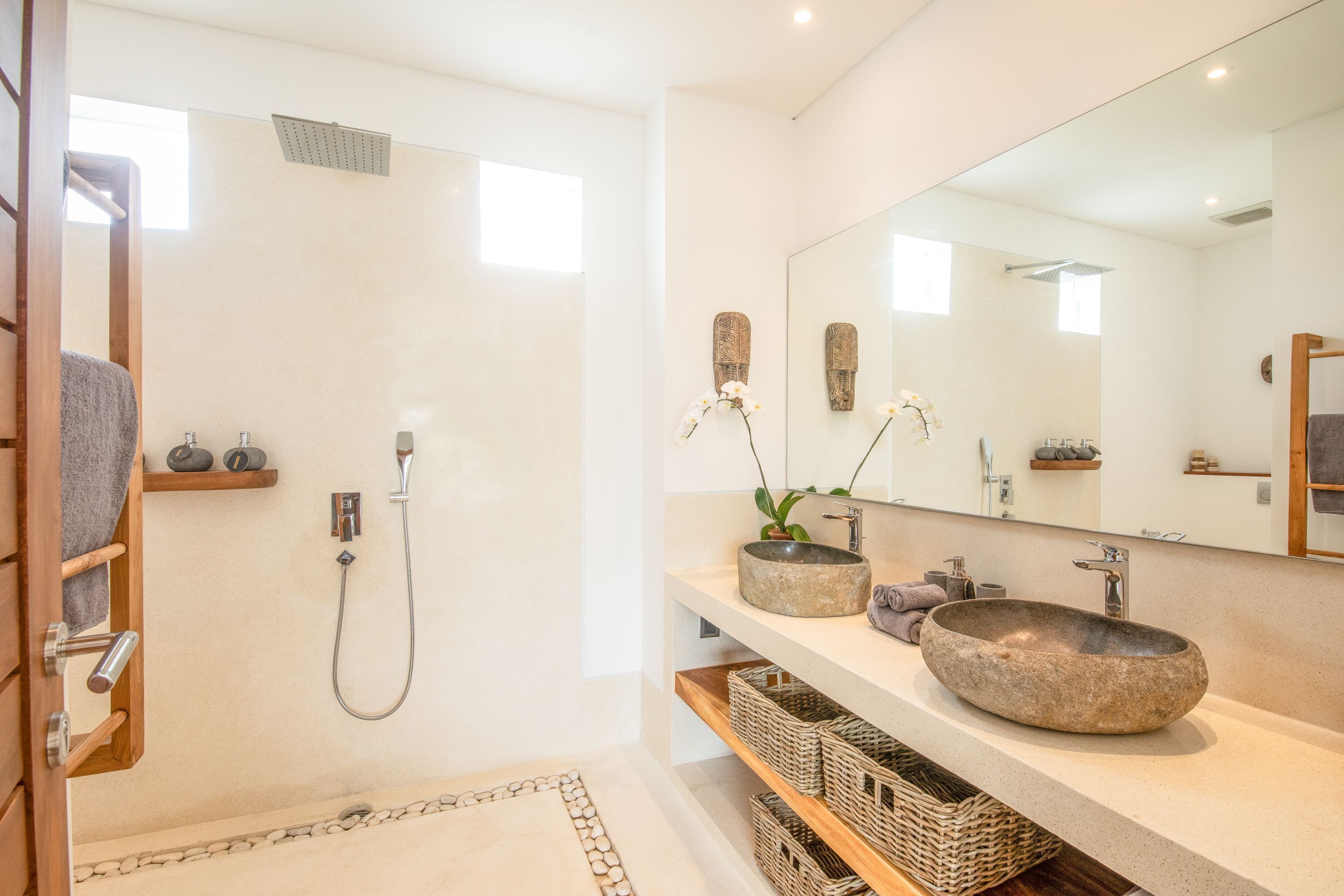 Une salle de bain moderne avec une douche à l’italienne, deux vasques en pierre, un grand miroir et des paniers en osier.