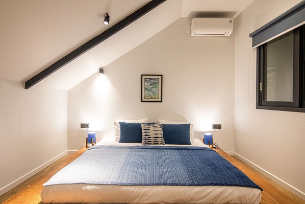 A bedroom with a sloped ceiling, a bed with a blue and white bedspread, two bedside lamps, and a framed picture on the wall. - Clifftop Villa 5 Mins to Bingin (Pecatu)
