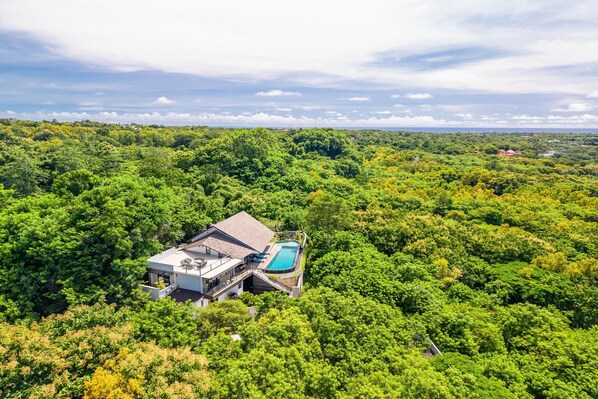 Une maison entourée d’une forêt dense, avec une piscine.
