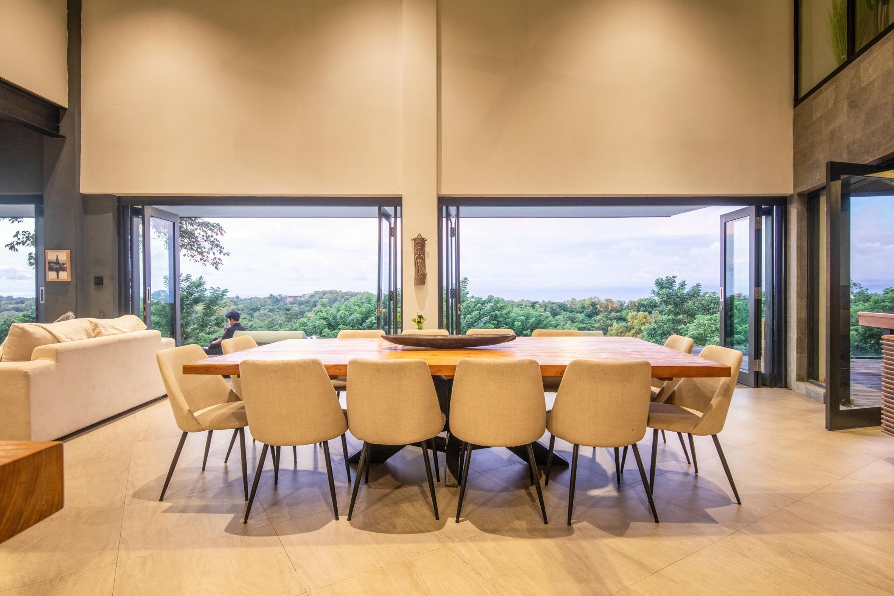 A modern dining area with a large wooden table and six chairs, large windows offering a view of the outdoors.