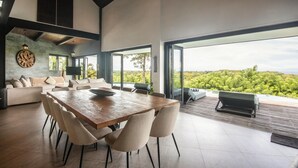 Ein moderner Essbereich mit Holztisch und -stühlen, einer Couch und einem großen Fenster mit Blick auf die Landschaft.