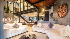 Ein geräumiger Wohnbereich mit zwei weißen Sofas, einem Couchtisch und einer Treppe, die in einen oberen Bereich führt.