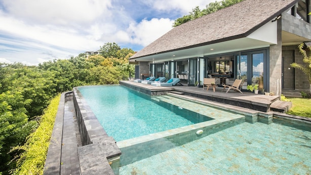 Ein modernes Haus mit großem Swimmingpool, Sitzgelegenheit im Freien und Blick auf die umliegende Grünfläche.