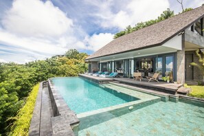 Une maison moderne dotée d’une grande piscine, d’un espace extérieur aménagé et offrant une vue sur la verdure environnante.