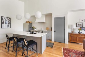 Eine moderne Küche mit einer zentralen Kochinsel, Barhocker, Pendelleuchten und einem Holzschrank.
