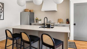 Une cuisine moderne dotée d’un grand îlot central, de tabourets de bar, de luminaires suspendus et d’un réfrigérateur.
