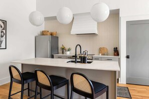 Una cocina moderna con una isla grande, taburetes de bar, luces colgantes y un refrigerador.