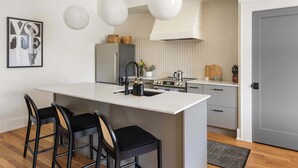 A modern kitchen with a central island, bar stools, pendant lights, and a refrigerator.