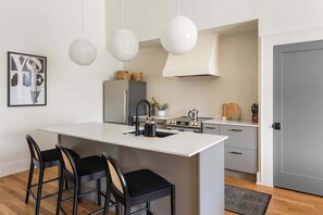 Een moderne keuken met een centraal eiland, barstoelen, hanglampen en een koelkast.