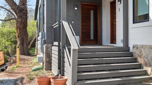 A modern house with a wooden door, grey exterior, and a small porch with steps leading to the entrance.