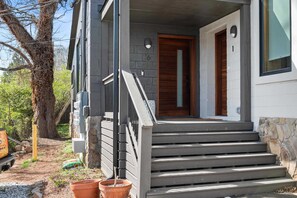Ein modernes Haus mit Holztür, grauer Fassade und einer kleinen Veranda mit Stufen zum Eingang.