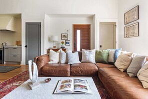 Ein Wohnzimmer mit einem braunen Ledersofa, einem Couchtisch mit einer Zeitschrift und einer Küche im Hintergrund.