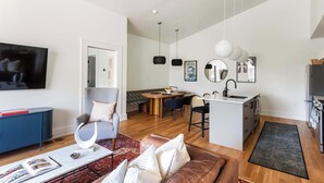 A modern living room with a TV, sofa, coffee table, and a dining area with chairs and a table.