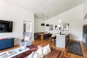Een moderne woonkamer met een televisie, bank, salontafel, en een eethoek met stoelen en een tafel.