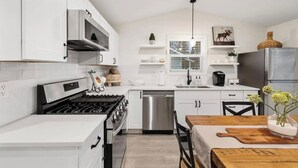 A modern kitchen with white cabinetry, a gas stove, stainless steel appliances, and a wooden dining table with a vase of flowers. - Freshly Updated Hideaway in CDA’s Best Spot (Coeur d'Alene)