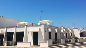 Un bâtiment moderne aux murs extérieurs blancs, doté de nombreux balcons et surmonté de parasols blancs.