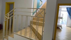 Un escalier avec une rampe blanche, une porte ornée d’un cadre turquoise et un sol carrelé.